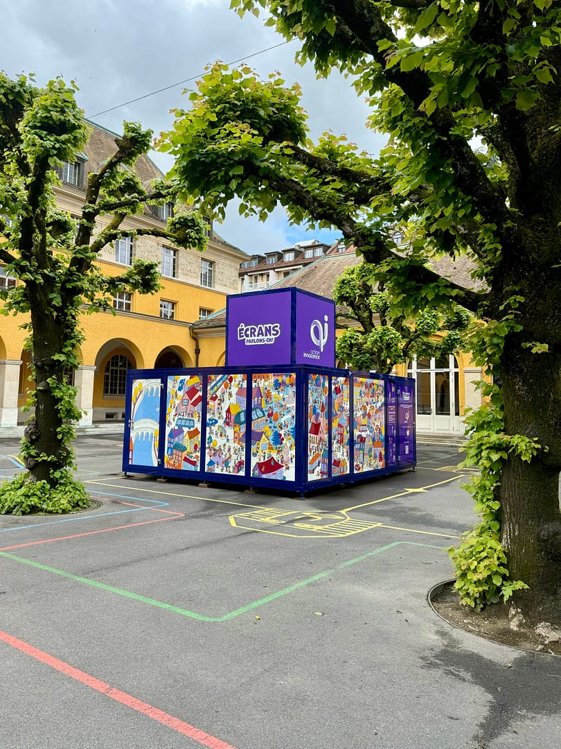 The Action Innocence traveling educational pavilion installed in an outdoor school courtyard, featuring colorful illustrated panels and branded signage, integrated into the environment beneath surrounding trees.