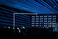 Wide view of the stage and audience during the Nansen Refugee Award – Hybrid Ceremony, with blue light beams, a branded UNHCR backdrop, and speakers addressing the crowd.