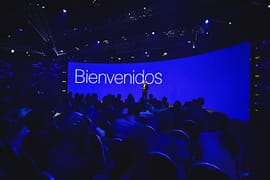 Speaker welcoming the audience on stage in front of a large blue screen reading “Bienvenidos” during the Conference in Buenos Aires – Immersive 360°.
