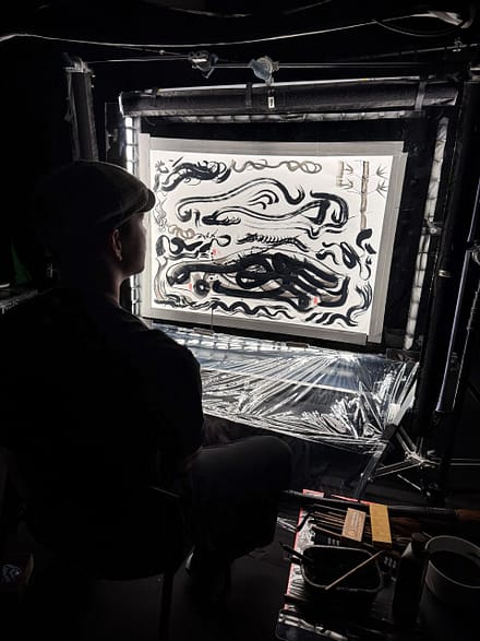 Artist observing a large ink artwork inside a backstage setup during the Mazda – Cinematic reveal of the Mazda 6E.